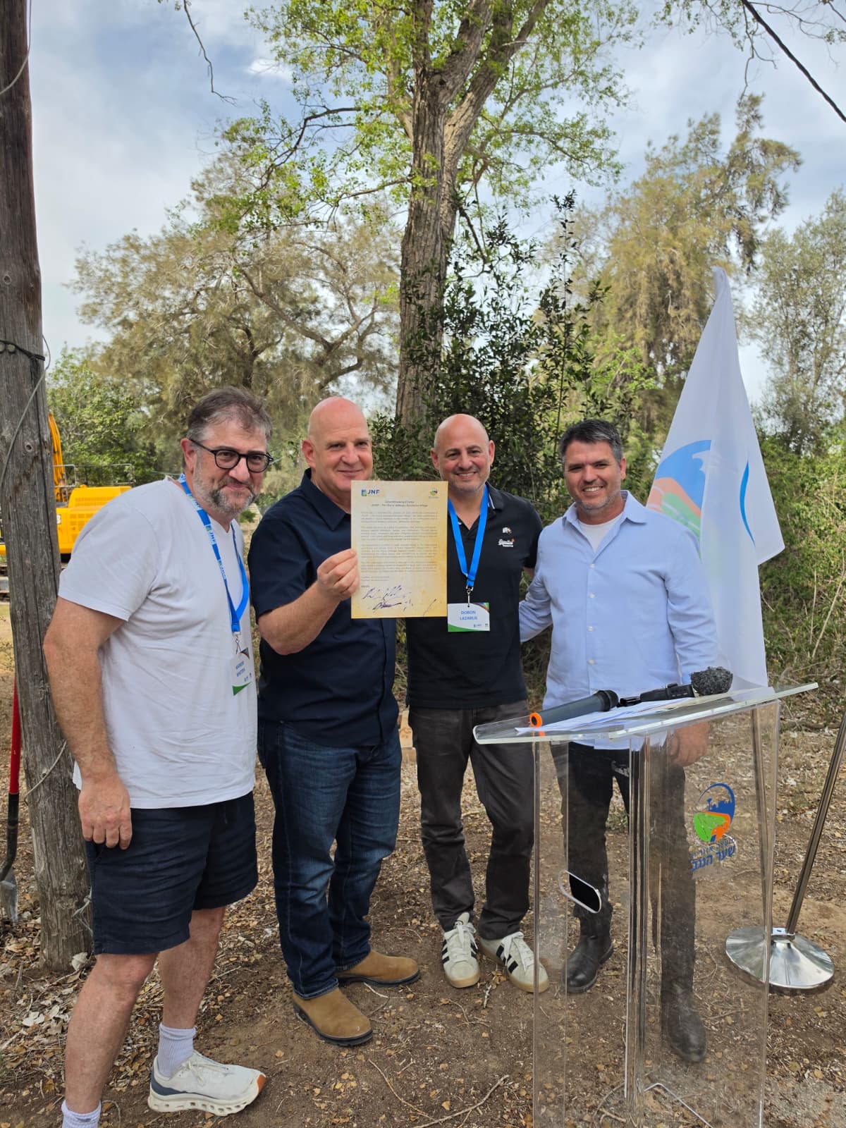 ארבעה משתתפים באירוע בשער הנגב, ליד דוכן נאומים; אחד מהם מציג מסמך